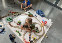 [fot. Katarzyna Waagner] Zajęcia w Centrum Aktywności Rodzin. Dwaj chłopcy bawią się wagonikami kolejowymi na ułożonych na macie torach. - powiększ