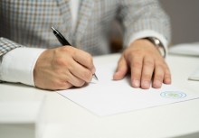 Zdjęcie dłoni trzymających długopis oraz podpisujących dokument - powiększ