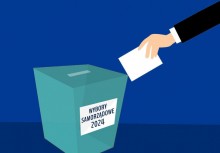 Na grafice dłoń trzymająca kartkę oraz urna wyborcza z napisem 'wybory samorządowe 2024' - powiększ