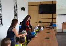 Wakacje z Urzędem Gminy Żukowo - Dzieci z Przedszkola z Miszewa w kamizelkach z opiekunkami, Sala konferencyjna Rady Miejskiej w Urzędzie Gminy w Żukowie, Pani Burmistrz Mariola Zmudzińska wita się i rozmawia z dziećmi. - powiększ