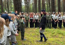 Na zdjęciu harcerze na zbiórce, jeden z chłopców melduje komendantce - powiększ