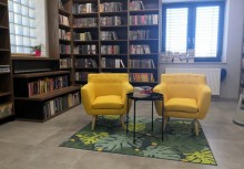 Pomieszczenie w bibliotece, dwa żółte fotele, w tle regał z książkami - powiększ