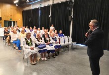 Mężczyzna przemawiający do siedzących na widowni kobiet w strojach kaszubskich - powiększ
