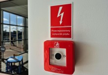 „Czerwony przycisk awaryjny z napisem Przeciwpożarowy wyłącznik prądu zamontowany na białej ścianie.” - powiększ