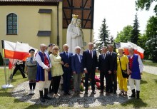 Kilka osób przed pomnikiem Matki Boskiej Królowej Polski, obok flagi Polski i Kaszub. W tle kościół pw. św. Jana w Żukowie - powiększ