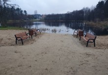 [fot. UG Żukowo] Ławki ustawione przy jeziorku w Żukowie. W tle widać drzewa. - powiększ