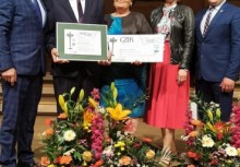 5 osób na scenie, Sołtys Tuchomia trzyma dyplom, przewodnicząca Koła Gospodyń Wiejskich w Tuchomiu trzyma symboliczny czek - powiększ