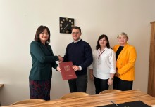 Uroczyste podpisanie dokumentu w Urzędzie Gminy w Żukowie.
Burmistrz Mariola Zmudzińska wręcza akt powierzenia nowemu dyrektorowi lub przedstawicielowi instytucji.
W tle dwie pracowniczki urzędu, całość w oficjalnym i eleganckim tonie - powiększ