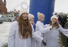 4 osoby, jedna trzyma mikrofon. W tle kościół - powiększ