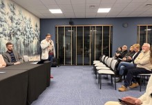 Na zdjęciu: po lewej przy stole prezydialnym siedzi jedna osoba, obok stołu stoi mężczyzna mówiący przez mikrofon, po prawej ok 6 osób na widowni podczas spotkania - powiększ