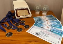 Na stole rozłożone są medale, dyplomy, statuetki i pamiątkowa tabliczka przyznane podczas międzynarodowego festiwalu Sea Sun Festival 2025 – nagrody zdobyte przez zespół Port Artówki z Polski. - powiększ