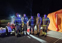 Strażacy stoją w nocy przy namiocie 