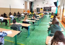 Uczniowie piszą test przy oddzielnych ławkach w sali gimnastycznej, z przodu widoczny baner konkursu. - powiększ