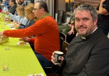 Ludzie w świetlicy siedzą przy stołach, na pierwszym planie proboszcz - powiększ