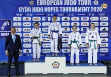 Cztery zawodniczkach w strojach do judo na podium. Obok stoi mężczyzna w garniturze. 