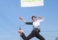 Na zdjęciu kobieta wykonuje skok w górę. Nad uczestniczką wisi baner Sołectwa Chwaszczyno.  - powiększ