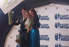 Na zdjęciu widoczne są  trzy kobiety stojące na podium. Każda z nich trzyma w dłoniach bukiet kwiatów.  - powiększ