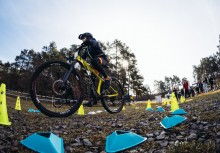 Uczestnik wyścigu jedzie na żółtym rowerze. W tle widać grupę kibiców oraz innych uczestników wyścigu.   - powiększ