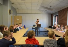 grupa dzieci siedząca przy stołach i przyglądająca się ramce pszczelarskiej prezentowanej przez kobietę - powiększ