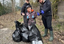 Na zdjęciu dwie dorosłe osoby i dziecko. Przed nimi czarne worki z zebranymi odpadami - powiększ