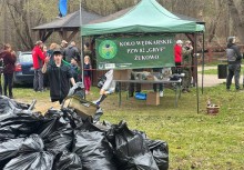 Na zdjęciu grupa osób. Po lewej stronie zdjęcia czarne worki wypełnione zebranymi odpadami. W centralnym punkcie zdjęcia baner.