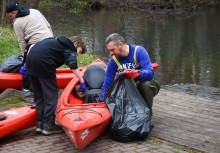 Na zdjęciu trzy osoby przy kajakach. Trzymają worki na odpady  - powiększ