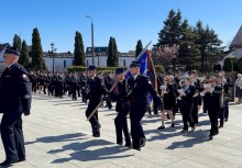 Przemarsz strażaków z pocztem sztandarowym oraz orkiestrą na placu podczas uroczystości.  - powiększ