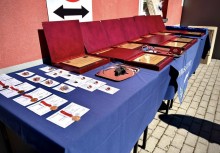 Stół przykryty niebieskim obrusem, na którym ułożono medale oraz pamiątkowe tabliczki.  - powiększ