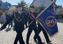 Poczet sztandarowy podczas przemarszu. W tle widać innych uczestników wydarzenia oraz budynki mieszkalne.  - powiększ