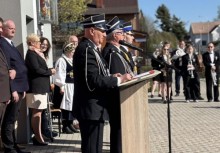 Strażak przy mównicy przemawia do mikrofonu. W tle widać innych uczestników wydarzenia.  - powiększ