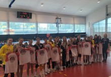 Zawodniczki UKS Banino pozują w hali sportowej z koszulkami pamiątkowymi i medalami po zdobyciu wicemistrzostwa Polski. W tle widoczna publiczność i tablica wyników - powiększ