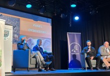 Panel dyskusyjny podczas konferencji – prelegenci rozmawiają na scenie o rozwoju lokalnym, w tle ekrany i banery organizatorów. - powiększ