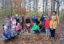 Na zdjęciu dzieci ze szkoły podstawowej z nauczycielką przed pomnikiem - powiększ