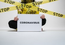 Na zdjęciu siedząca kobieta trzymające kartkę z napisem: 'coronavirus'. Dookoła taśmy z napisem: 'stop' - powiększ