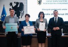 Na zdjęciu cztery osoby. Dwie kobiety i dwaj mężczyźni. W tle wyświetlona prezentacja z napisem 'Uroczyste podpisanie umów 'Pomorskie dla Zwierząt'.