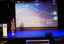 Prelegentka prezentuje temat o roli technologii w promowaniu dziedzictwa kulturowego na scenie z dużym ekranem i napisem „Tradycja i nowoczesność…”. - powiększ