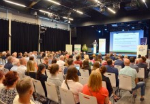 Sala wypełniona uczestnikami konferencji – prelegent prezentuje slajdy na temat rozwoju lokalnego, w tle banery promujące region i partnerów wydarzenia. - powiększ