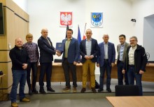 8 osób stoi w sali Rady Miejskiej w Urzędzie Gminy w Żukowie, burmistrz trzyma teczkę z umową - powiększ