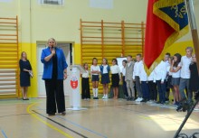 Dyrektor szkoły przemawia podczas uroczystości z udziałem pocztu sztandarowego – uczniowie ustawieni w szeregu w sali gimnastycznej. - powiększ