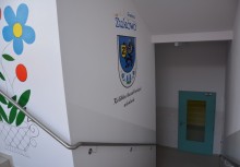 Na zdjęciu schody w szkole w Tuchomiu, na ścianie herb Żukowa i napis 'Żukowo' oraz napis po kaszubsku 'Kolebka haftu kaszubskiego' - powiększ