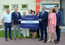 9 osób przed szkołą w Tuchomiu, Burmistrz Gminy Żukowo i Wiceminister Funduszy i Polityki Regionalnej trzymają symboliczny czek z kwotą 1 955 000 zł 