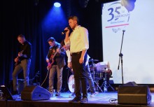 Występ zespołu muzycznego podczas gali 35-lecia samorządu – wokalista z mikrofonem na pierwszym planie, w tle grający instrumentaliści i ekran z logo wydarzenia. - powiększ