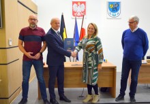 4 osoby, w tle flagi Kaszub, Unii Europejskiej i Polski. Burmistrz trzyma teczkę z umową - powiększ