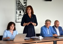 Zdjęcie przedstawia kobietę stojącą przy stole konferencyjnym, wygłaszającą wypowiedź podczas spotkania. Obok niej siedzą trzy osoby, w tle widoczna grafika z napisem „Wendelstein”. Atmosfera oficjalna. - powiększ