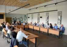Zdjęcie przedstawia spotkanie w sali konferencyjnej – uczestnicy siedzą przy dużym, podłużnym stole. W tle dekoracje ścienne i elementy graficzne. Atmosfera formalna, robocza