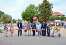 11 osób, przecięcie wstęgi, w tle plac zabaw i dzieci - powiększ