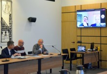 3 osoby w sali Rady Miejskiej w Urzędzie Gminy Żukowie, na ekranie telewizora dodatkowo dwie osoby - powiększ