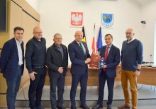 6 osób w sali obrad Rady Miejskiej w Urzędzie Gminy w Żukowie. Burmistrz i wykonawca inwestycji trzymają teczkę