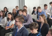 Uczniowie na konferencji lub warsztatach – młodzież w formalnych strojach z identyfikatorami na smyczach, skupiona podczas spotkania edukacyjnego w sali wykładowej.