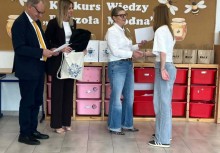 Na zdjęciu cztery osoby: trzy kobiety i mężczyzna. Jedna z kobiet gratuluje uczestniczce konkursu. W tle tablica korkowa z napisem 'I Wojewódzki Konkurs Wiedzy - Pszczoła Miodna'. - powiększ